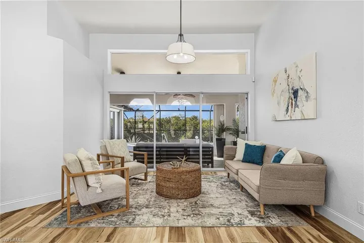 Living area featuring a sunroom, wood finished floors, a towering ceiling, and a textured wall