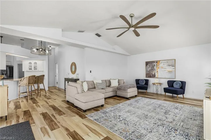 Living room featuring light wood-style flooring, lofted ceiling, a ceiling fan, and a chandelier
