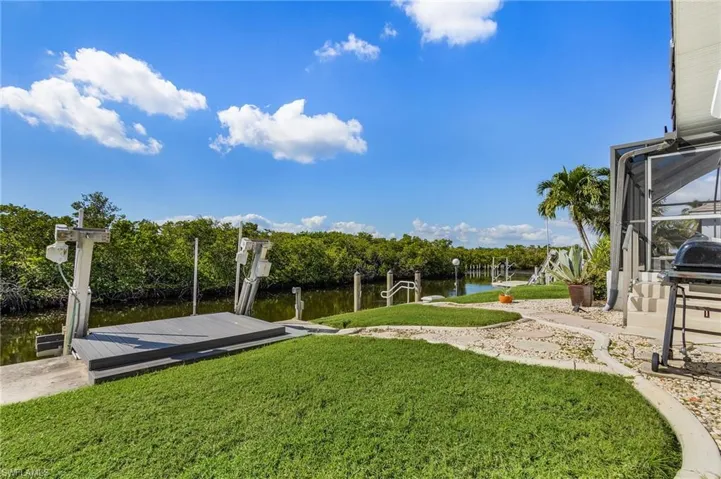 View of grassy yard featuring a water view, a dock, boat lift, and a lanai