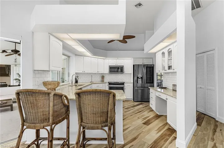 Kitchen with ceiling fan, light stone countertops, appliances with stainless steel finishes, and white cabinetry