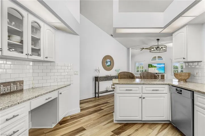 Kitchen with backsplash, dishwasher, light stone counters, and white cabinets