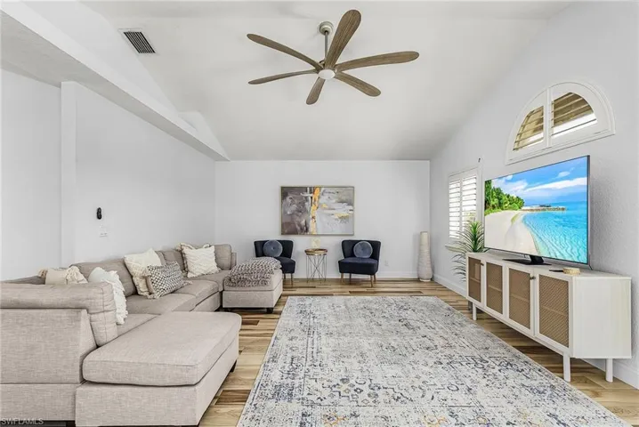 Living room with ceiling fan, light wood finished floors, and lofted ceiling
