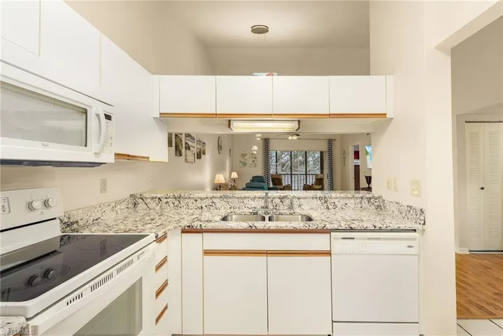 Kitchen featuring white appliances, white cabinets, light stone counters, and open floor plan