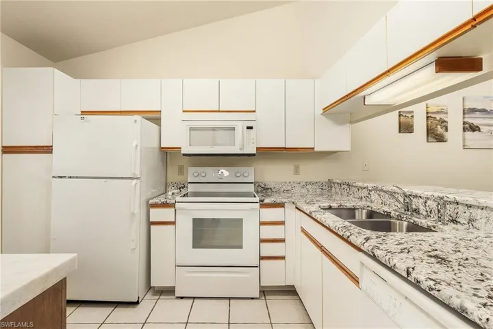 Kitchen with white appliances, white cabinets, light tile patterned floors, lofted ceiling, and light stone counters