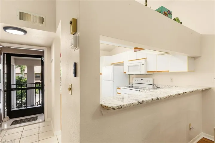 Kitchen featuring white appliances, white cabinetry, a peninsula, light tile patterned floors, and light stone counters