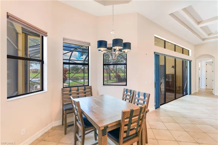 Dining room with coffered ceiling, light tile flooring, a raised ceiling, and an inviting chandelier
