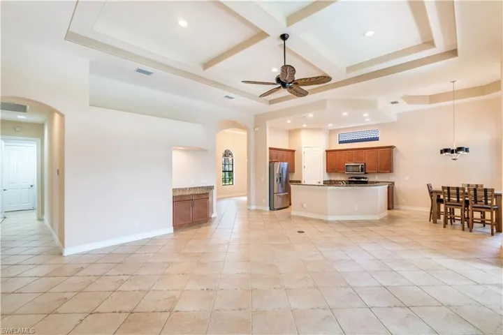 Living room with beamed ceiling, coffered ceiling, light tile flooring, ceiling fan, and a raised ceiling