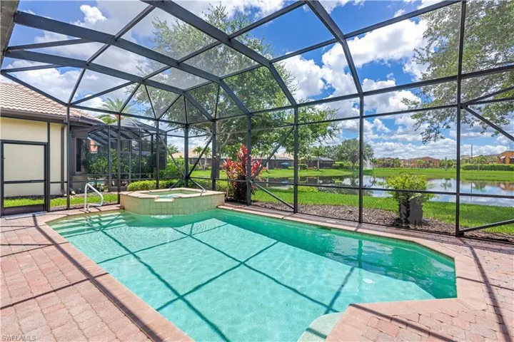 View of swimming pool featuring glass enclosure, a water view, an in ground hot tub, and a patio area