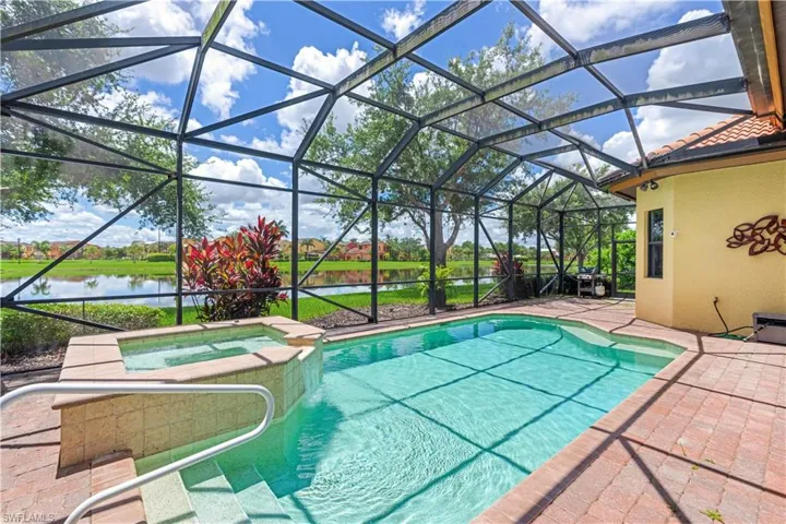 View of pool featuring a patio area, glass enclosure, an in ground hot tub, and a water view