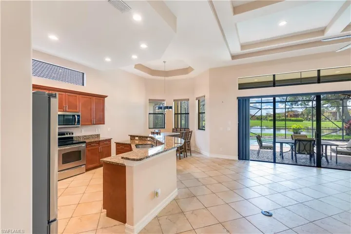 Kitchen featuring light stone countertops, stainless steel appliances, sink, light tile flooring, and a raised ceiling