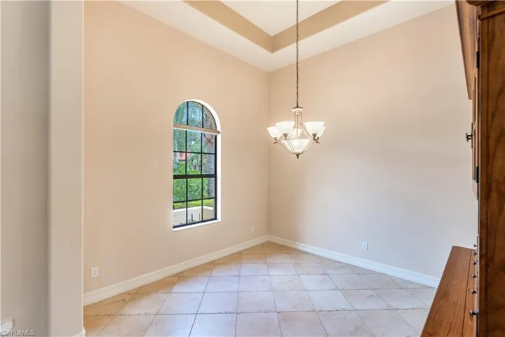 Empty room with a notable chandelier, a high ceiling, light tile flooring, and a tray ceiling