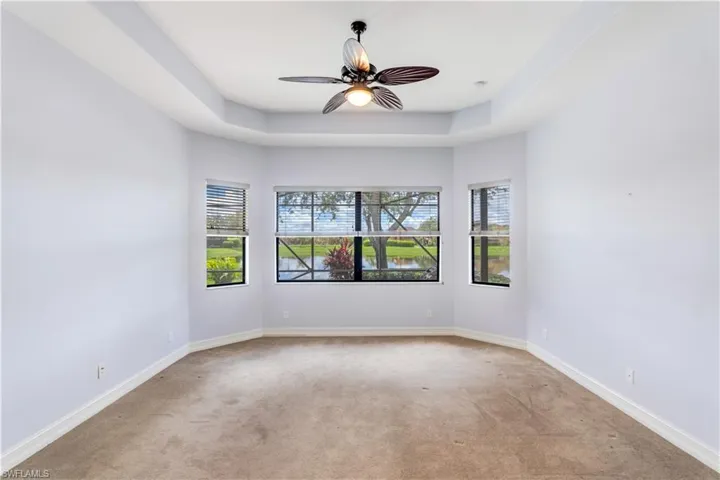Empty room with ceiling fan, light colored carpet, and a raised ceiling