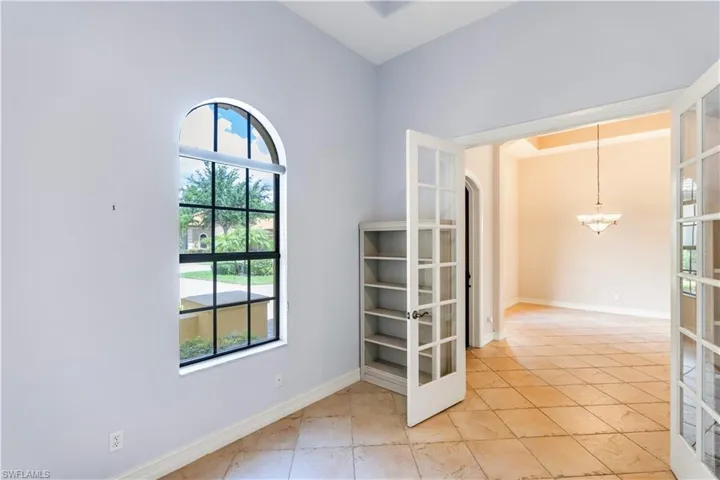 Spare room featuring french doors, light tile flooring, and an inviting chandelier