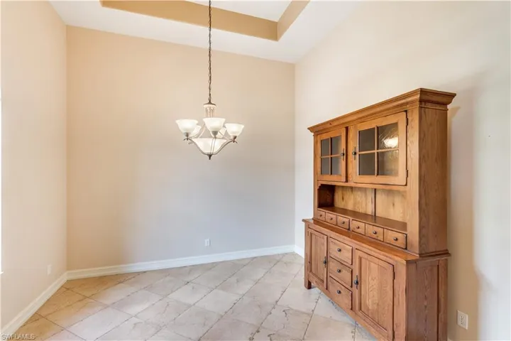 Unfurnished dining area with an inviting chandelier, a tray ceiling, and light tile floors