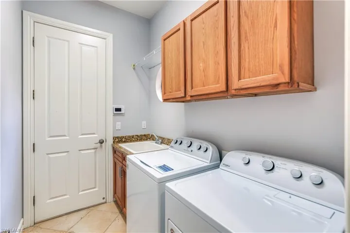 Clothes washing area featuring sink, light tile flooring, independent washer and dryer, and cabinets