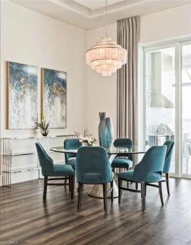 Dining area with dark wood finished floors, a chandelier, and a raised ceiling