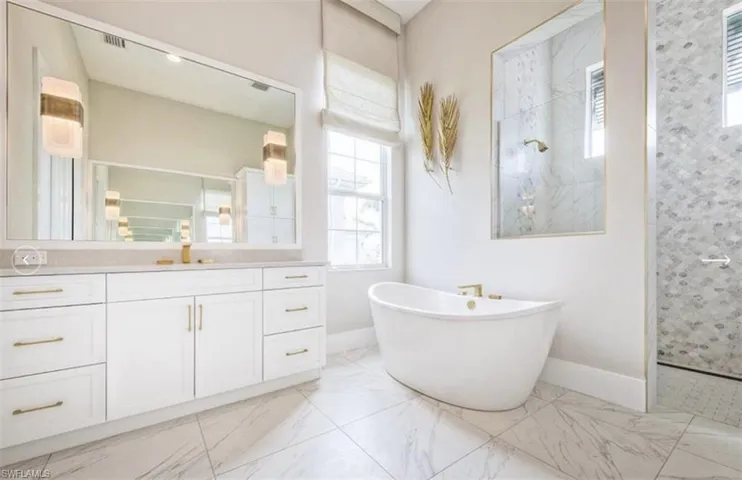 Full bath with a walk in shower, vanity, a freestanding bath, and light marble finish flooring