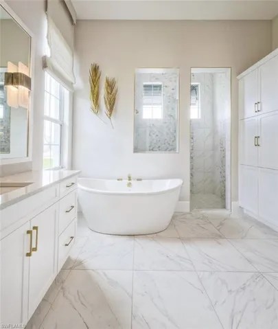 Bathroom with a freestanding bath, vanity, a marble finish shower, and light marble finish flooring