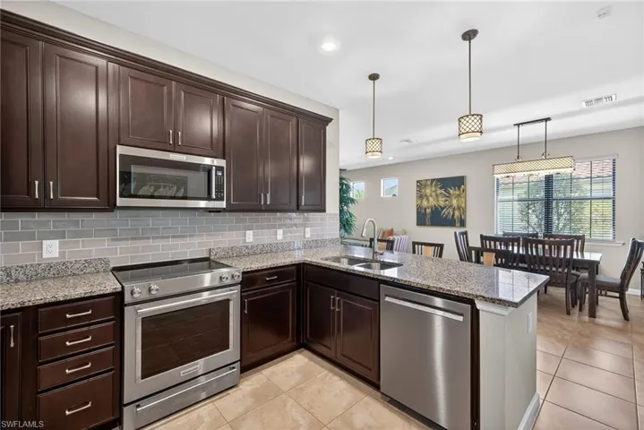 Kitchen with dark brown cabinets, appliances with stainless steel finishes, light stone countertops, light tile patterned floors, and recessed lighting