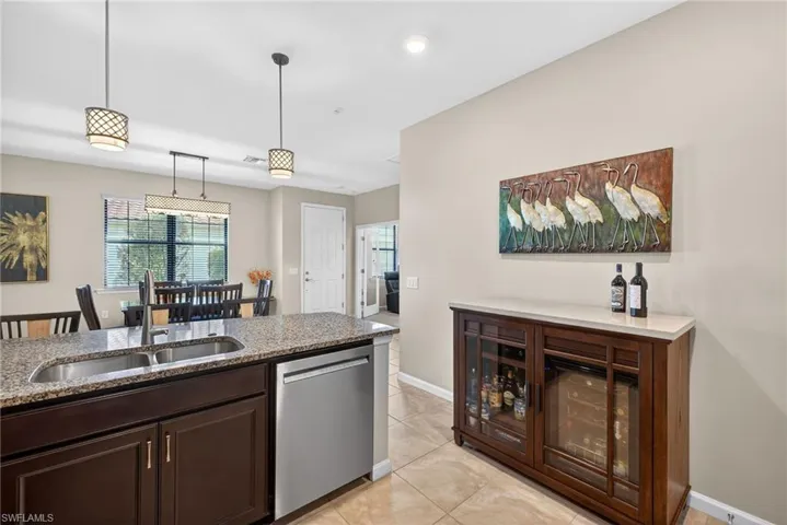 Kitchen with dark brown cabinetry, dishwasher, hanging light fixtures, light stone counters, and light tile patterned floors
