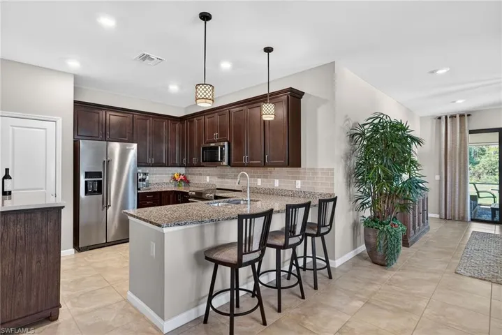 Kitchen with dark brown cabinets, appliances with stainless steel finishes, a breakfast bar area, light stone countertops, and decorative light fixtures