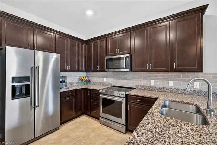 Kitchen featuring stainless steel appliances, dark brown cabinets, light stone countertops, tasteful backsplash, and light tile patterned floors