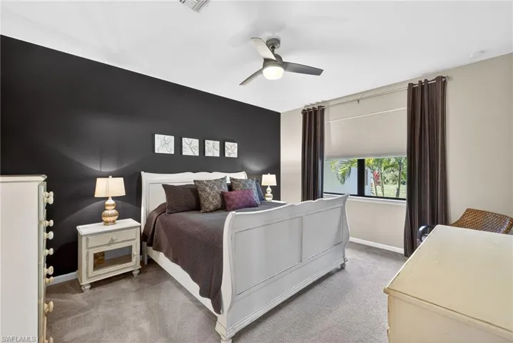 Bedroom with light colored carpet, an accent wall, and ceiling fan