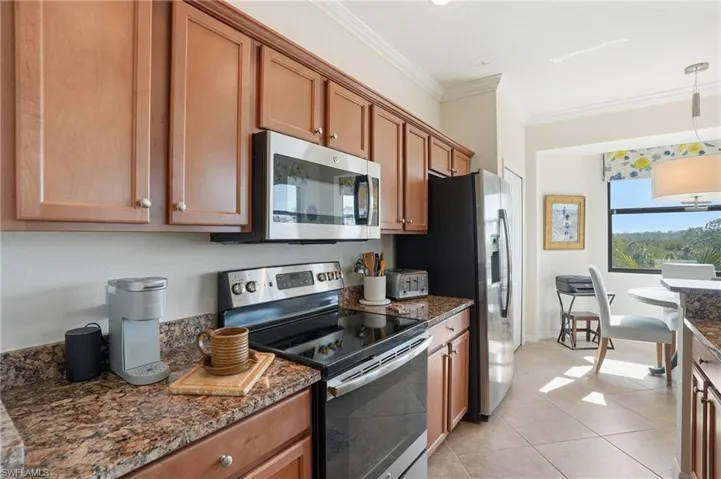 Kitchen featuring stainless steel appliances, crown molding, hanging light fixtures, dark stone countertops, and wood finish cabinetry
