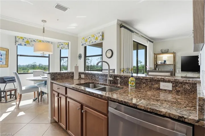 Kitchen with dishwasher, hanging light fixtures, dark stone countertops, ornamental molding, and wood finish cabinets