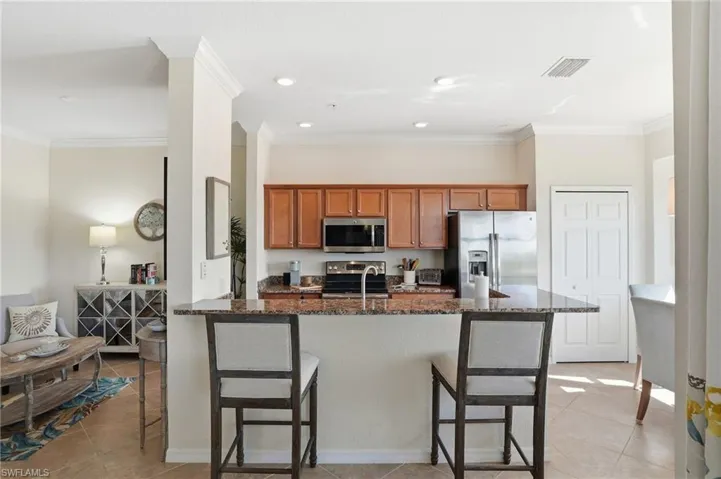 Kitchen featuring wood finish cabinetry, a breakfast bar, crown molding, dark stone counters, and stainless steel appliances