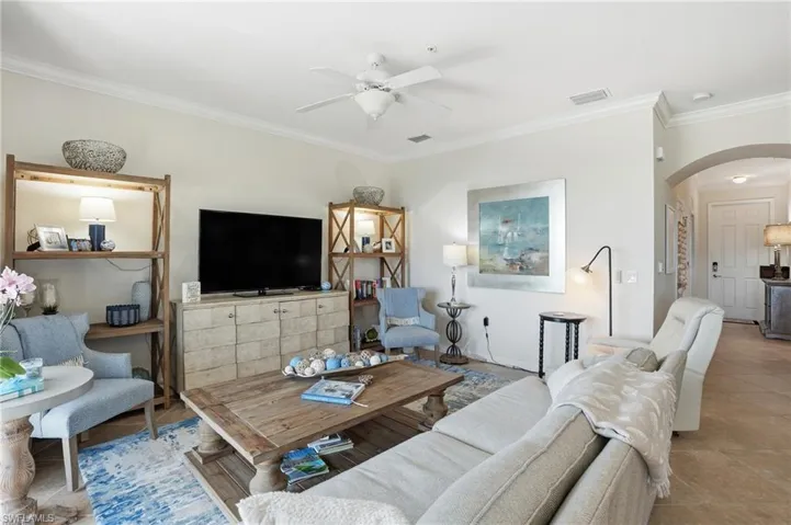 Living room featuring arched walkways, ornamental molding, a ceiling fan, and tile patterned flooring