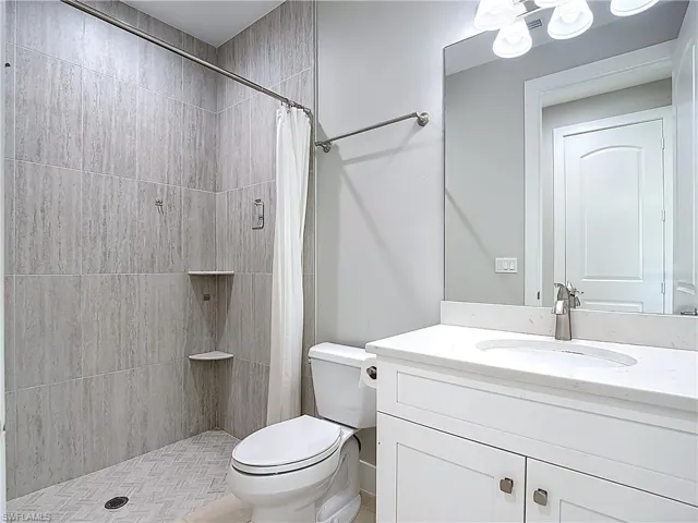 This bathroom features a contemporary vanity with a white countertop and basin, a large mirror, and a tiled shower area with built-in corner shelves