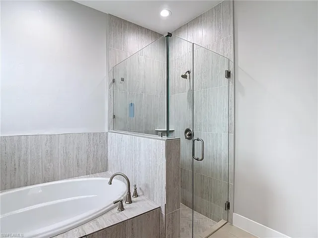 Master bathroom featuring a built-in bathtub with brushed nickel fixtures, a glass-enclosed shower with a rainfall showerhead, and light-colored tile work