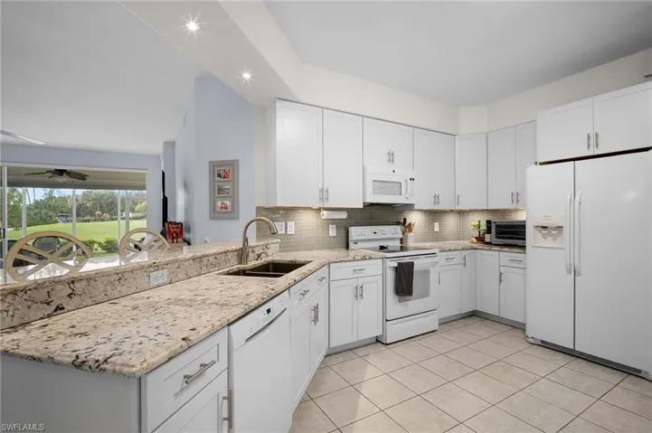 Kitchen with white appliances, light stone countertops, a peninsula, white cabinets, and decorative backsplash