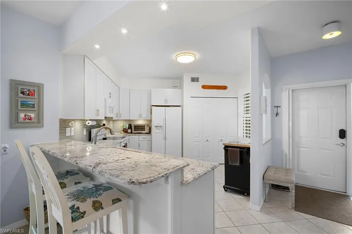 Kitchen featuring light stone countertops, white cabinets, white appliances, a peninsula, and a kitchen bar