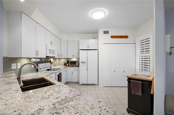 Kitchen featuring white appliances, white cabinets, light stone counters, light tile patterned floors, and decorative backsplash