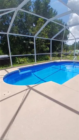 Outdoor pool with a sunroom, glass enclosure, and a patio