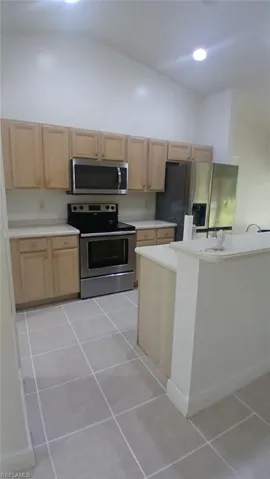 Kitchen featuring light wood finish cabinets, light countertops, stainless steel appliances, light tile patterned floors, and lofted ceiling