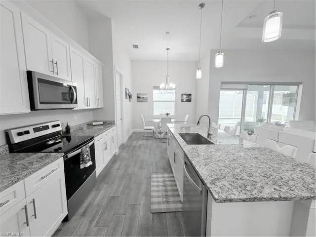 Kitchen with stove, light wood-style floors, dishwashing machine, a chandelier, and an island with sink