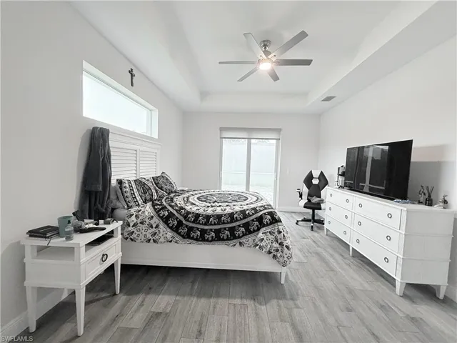 Living area featuring light wood-type flooring, a ceiling fan, a high ceiling, a raised ceiling, and recessed lighting