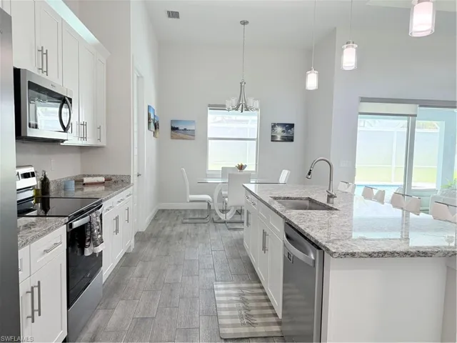 Kitchen with range, dishwasher, light wood-style flooring, a kitchen island with sink, and white cabinetry