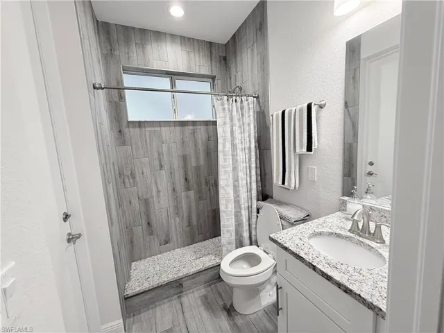 Bathroom featuring tiled shower, vanity, a textured wall, and wood finished floors