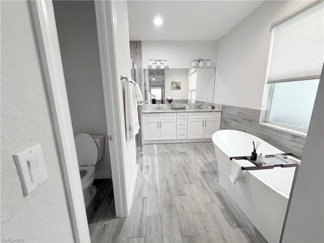 Full bath with a freestanding tub, double vanity, wood finished floors, and tile walls
