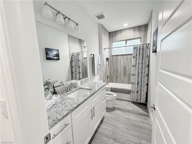 Bathroom featuring vanity, shower / bath combination with curtain, and recessed lighting