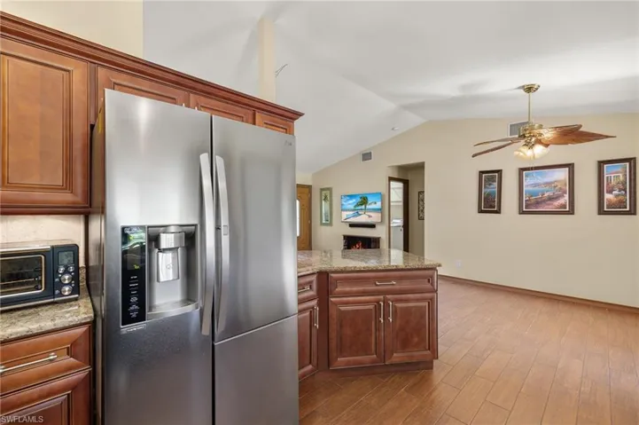 Kitchen with ceiling fan, light stone counters, stainless steel fridge with ice dispenser, light hardwood / wood-style floors, and lofted ceiling