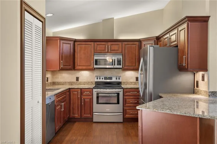 Kitchen featuring stainless steel appliances, light stone counters, dark hardwood / wood-style flooring, lofted ceiling, and decorative backsplash