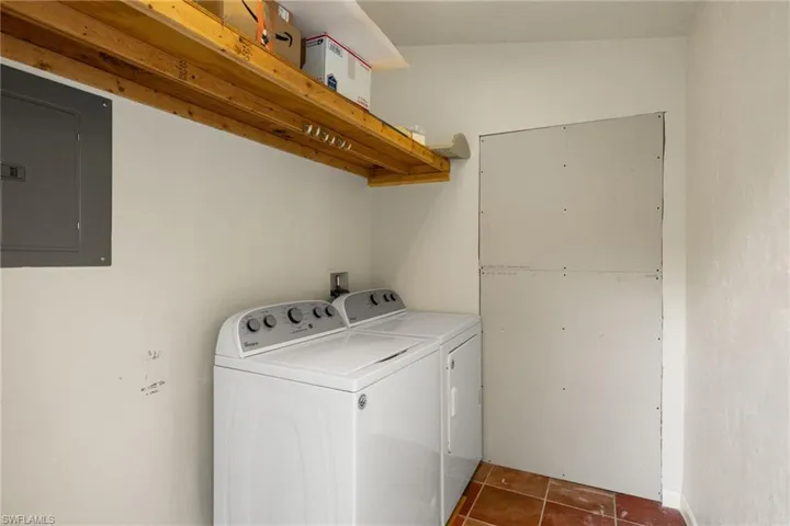 Laundry area with electric panel, washer and dryer, and dark tile patterned flooring