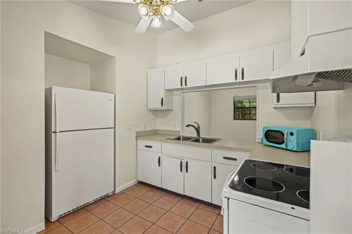 Kitchen with white cabinetry, sink, ceiling fan, white appliances, and light tile patterned floors