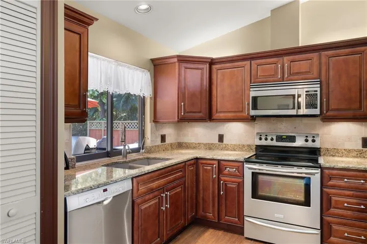 Kitchen featuring decorative backsplash, light wood-type flooring, stainless steel appliances, vaulted ceiling, and sink