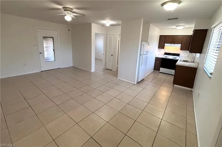 Kitchen featuring light countertops, dark wood finish cabinetry, white appliances, light tile patterned floors, and ceiling fan